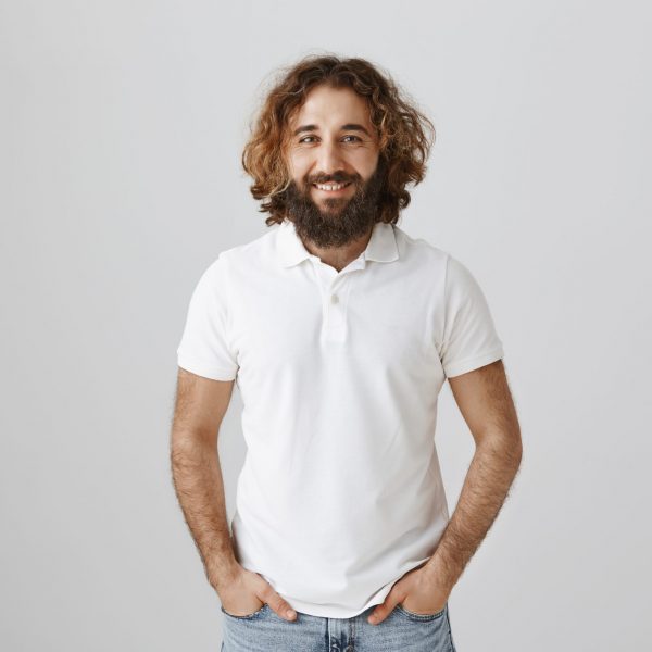 Eastern businessman in white shirt standing in confident pose with hands in pockets, ready to sign deal and arrange meeting with business partners, standing self-assured over gray wall.