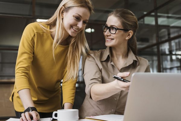 zwei-smiley-geschaftsfrauen-die-mit-laptop-am-schreibtisch-arbeiten
